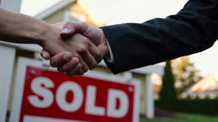Real estate transaction is finalized as agent and client shake hands, celebrating successful home purchase in front of sold sign, captured in slow motion