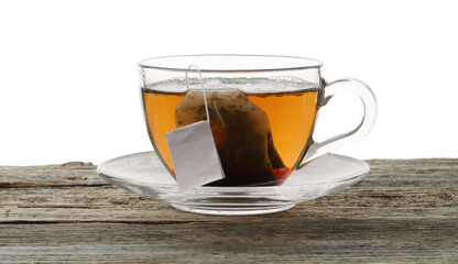 Tea bag in glass cup with hot drink on wooden table against white background