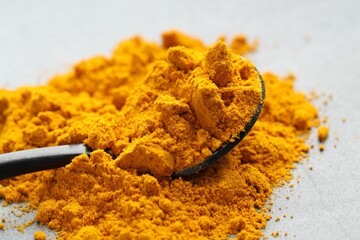 Turmeric powder and spoon on grey table, closeup
