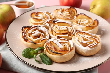 Tasty apple roses with powdered sugar served on pink table, closeup