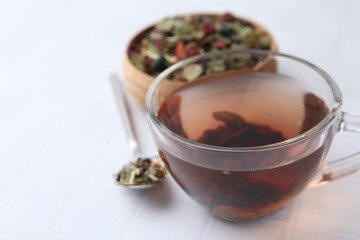 Delicious herbal tea and dry leaves on white tiled table, closeup