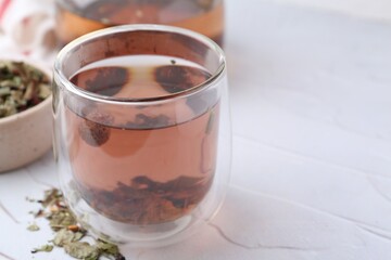 Delicious herbal tea and dry leaves on white table, closeup. Space for text