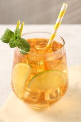 Refreshing iced tea with slices of lime, mint and drinking straw in glass on light table against grey background, closeup