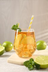 Refreshing iced tea with slices of lime, mint and drinking straw in glass on light textured table against grey background