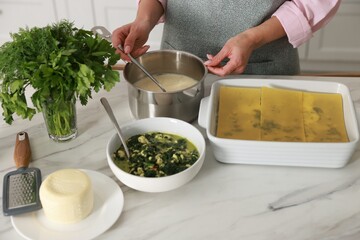 Woman making spinach lasagna at marble table indoors, closeup