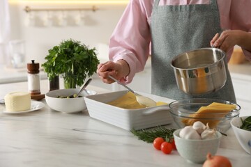 Woman spreading bechamel sauce onto spinach lasagna at marble table indoors, closeup