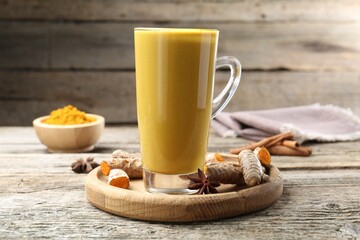 Delicious turmeric latte in glass cup, roots and spices on wooden table, closeup