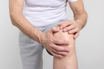 Senior man suffering from knee pain on light grey background, closeup