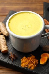 Tasty turmeric latte in cup and spices on wooden table, closeup