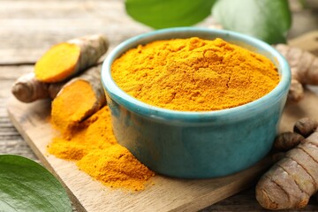 Turmeric powder in bowl and roots on table, closeup