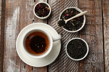 Aromatic tea and dried leaves on wooden table, flat lay