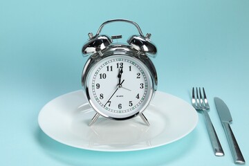 Alarm clock, plate and cutlery on light blue background