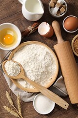 Rolling pin and ingredients for dough on wooden table, flat lay