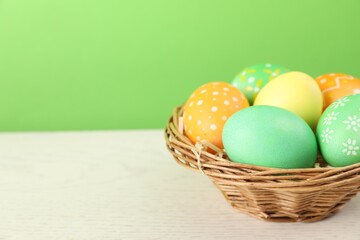 Many decorated Easter eggs in wicker basket on wooden table against light green background, closeup. Space for text