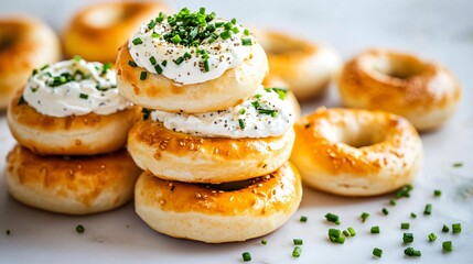 A stack of mini bagels with whipped herb cream cheese between each layer, topped with fresh chives, isolated on a light marble surface