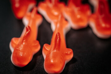 A close-up of several red gummy shark candies with a white base arranged on a black surface. The...