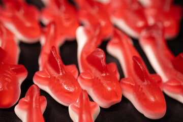 A close-up of several red gummy shark candies with a white base arranged on a black surface. The...
