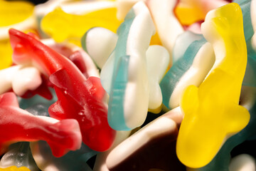 A close-up of multi-colored gummy shark candies in red, yellow, blue and white. The candies have a shiny, translucent texture and are stacked together, creating a lively display.