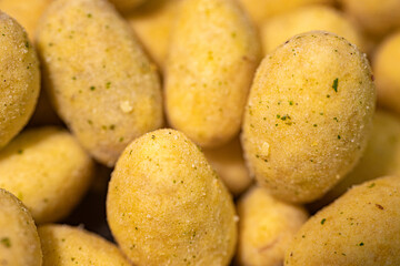 A macro shot of crunchy, spice-coated peanuts with a golden yellow hue. The textured surface highlights their crunchy coating, making them a tasty snack option.