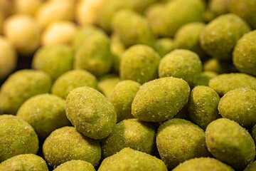 A detailed close-up of two varieties of peanuts, one with a green spice and the other with a yellow coating. The contrasting colors and textures highlight this crunchy snack.