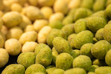 A detailed close-up of two varieties of peanuts, one with a green spice and the other with a yellow coating. The contrasting colors and textures highlight this crunchy snack.