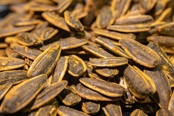 A detailed close-up of roasted sunflower seeds coated with spices. The seeds have a dark, textured shell with a golden layer of spices that highlight their rich flavor and crunchy texture.