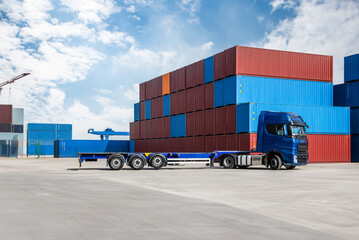 A blue semi truck is parked in front of a stack of blue and red containers