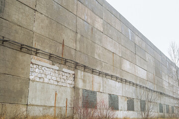 Old worn out facade of a long multi-span industrial building workshop. Wall made of unprotected...