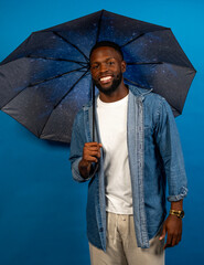 Cheerful man holding umbrella with galaxy design smiling on blue background