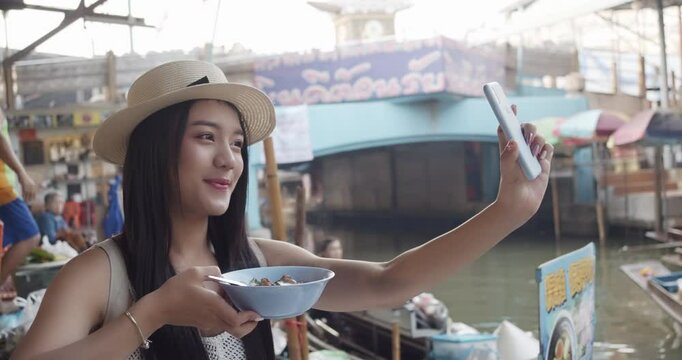 Young Asian tourist woman cheerful and happy to eat street food and sight seeing travel by boat along the canel at Damnoen Saduak Floating Market Thailand