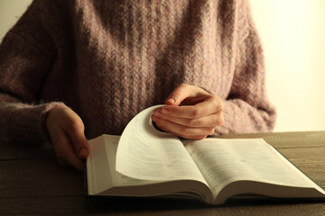 Woman reading Holy Bible at wooden table, closeup