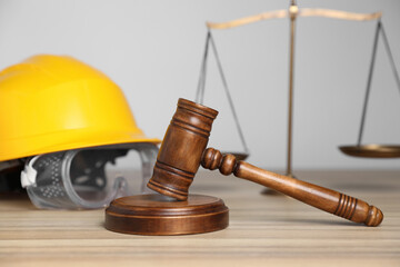 Accident at work concept. Gavel, scales and construction worker's protective gear on wooden table, selective focus