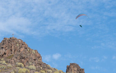 Paraglider soaring through the blue sky near towering rocks