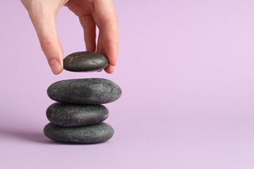 Harmony and life balance. Woman making stack of stones on lilac background, closeup. Space for text