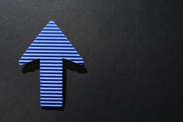 One blue paper arrow on black background, top view. Space for text