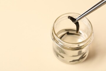 Taking medicinal leech from jar with tweezers on pale yellow background, closeup. Space for text