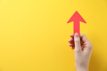 Woman with paper arrow on yellow background, top view. Space for text