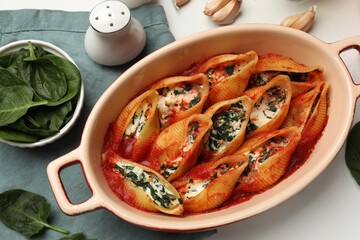 Delicious conchiglie pasta with ricotta cheese, spinach and tomato sauce in baking dish on white...