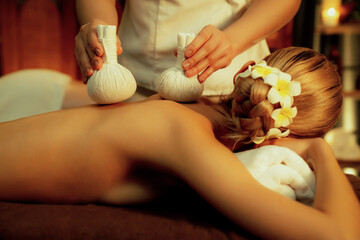 Hot herbal ball spa massage body treatment, masseur gently compresses herb bag on couple customer...