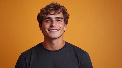 Fototapeta premium young stylish man in a black t-shirt smiling and standing in front of an orange background, portrait photography of a confident male model with a trendy outfit and charming expression in a studio sett
