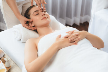 Caucasian woman enjoying relaxing anti-stress head massage and pampering facial beauty skin recreation leisure in dayspa modern light ambient at luxury resort or hotel spa salon. Quiescent