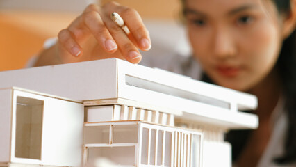Closeup image of skilled architect engineer hand pointing at house model to measure house length. Asian project manager hand using pencil marking at architectural model. Business design. Manipulator.