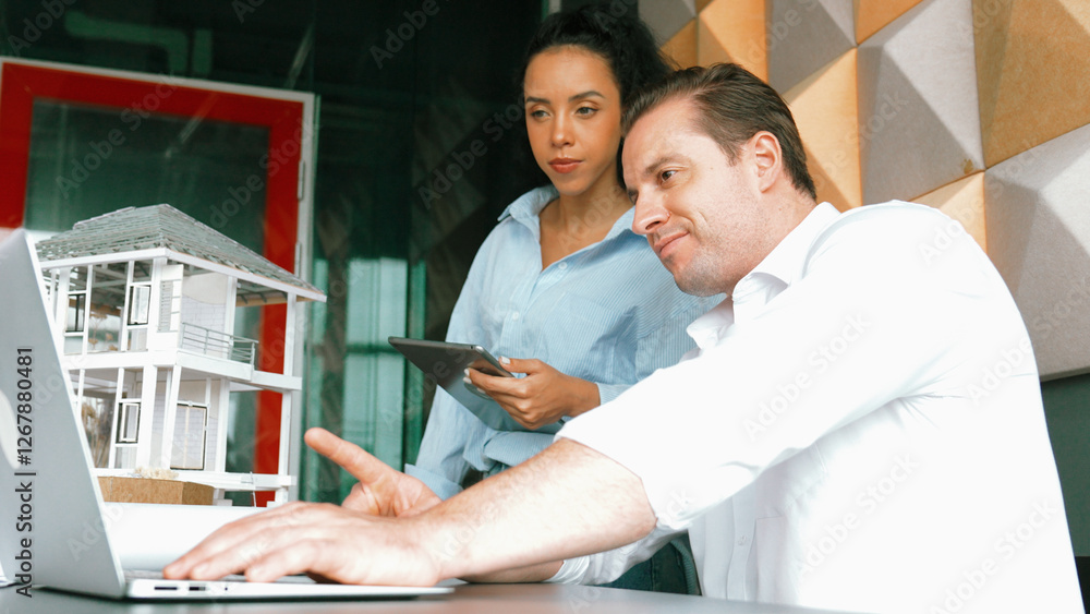 Poster portrait of project manager pointing at house model while discussion about building design. caucasia