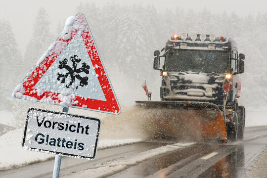 Vor einem Fahrzeug f&uuml;r Winterdienst und Schneer&auml;umung steht ein Verkehrsschild und warnt vor Glatteis - FOTOMONTAGE