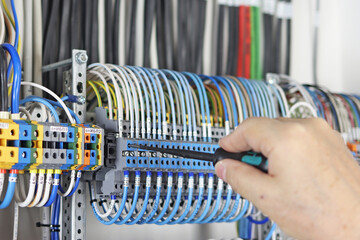 A hand with a screwdriver connects the insulated wiring wires to the modules in the switchboard. 