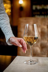 Elegant Hand Holding a Glass of White Wine in a Cozy Restaurant Setting