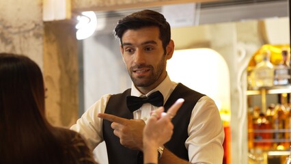 Smiling smart bartender providing excellent service to beautiful guest woman at back side vibrant nightlife party atmosphere in engaging lively conversation with VIP customer at nightclub . Vinosity.