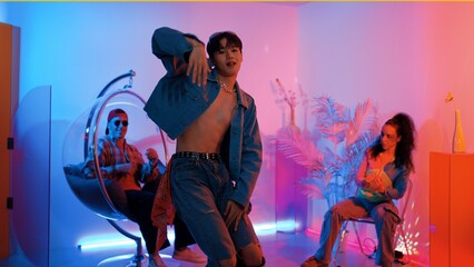 Fototapeta premium Skilled asian dancer moving to modern music while multicultural friend sitting at chair. Professional performer dancing show energetic foot step while hipster team cheering and supporting. Regalement.