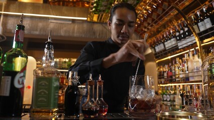 Smart Asian bartender using stirring mixed alcohol syrup into glass with ice for on the rock served...