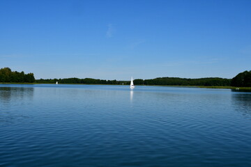 A view of a vast yet shallow river surrounded from all sides with shrubs, reeds, trees, forests, and moors spotted on a cloudy summer day with numerous boats and kayaks sailing it for sport